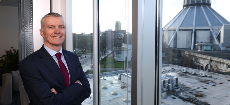 man with arms folded standing in front of window