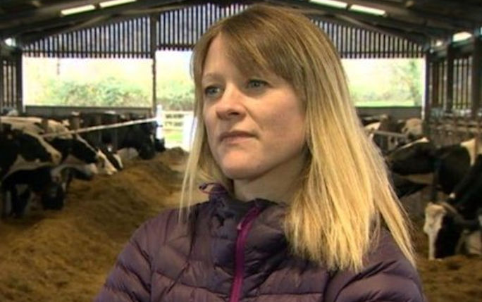 A headshot of Gwen wearing a purple coat stood in a cow barn