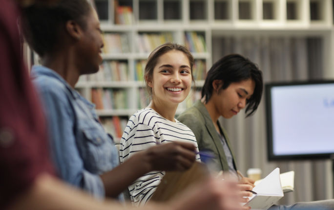 A group of students sit in a library smiling 