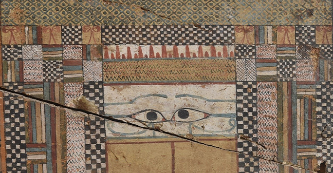 Detail of the front side of a coffin featuring ancient Egyptian illustrated eyes and colourful patterns