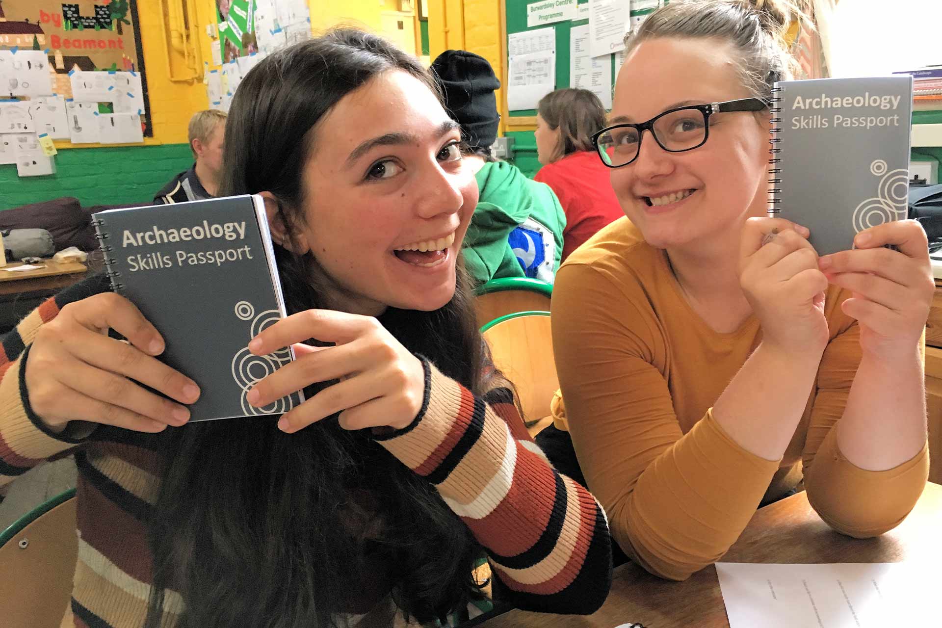 Two students smiling and holding up a book entitled Archaeology Skills Handbook