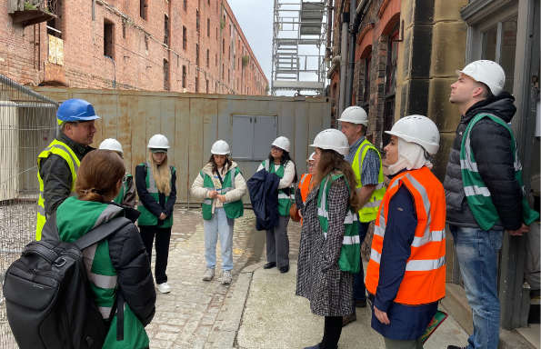 Group of people wearing PPE on a building site. A High brick built warehouse is being restored around them.