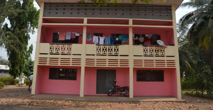 Indian two story house. Washing hangs from the first floor veranda, a scooter is parked by the front door.