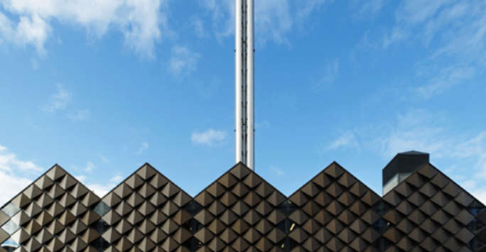 A building with a pitched roof and a bronze diamond block facade, a metal chimney behind the building.