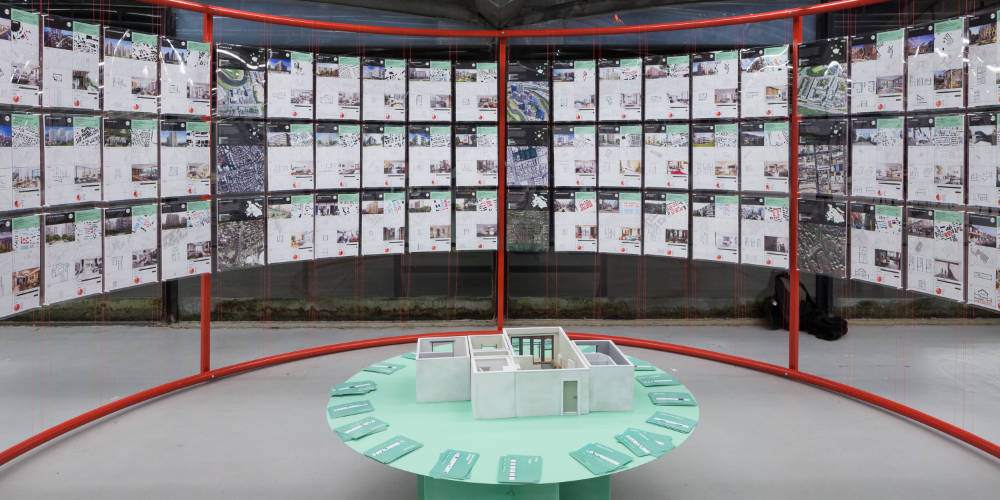 Circular table with a model of modern apartment on it. The table is surrounded by display boards showing modern housing typologies around the world.