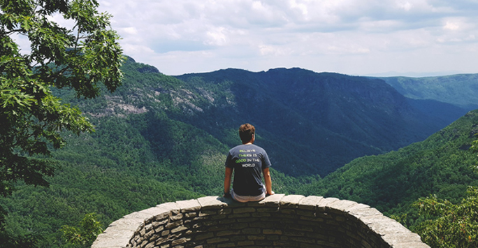 Man sitting looking at green landscape in the distance