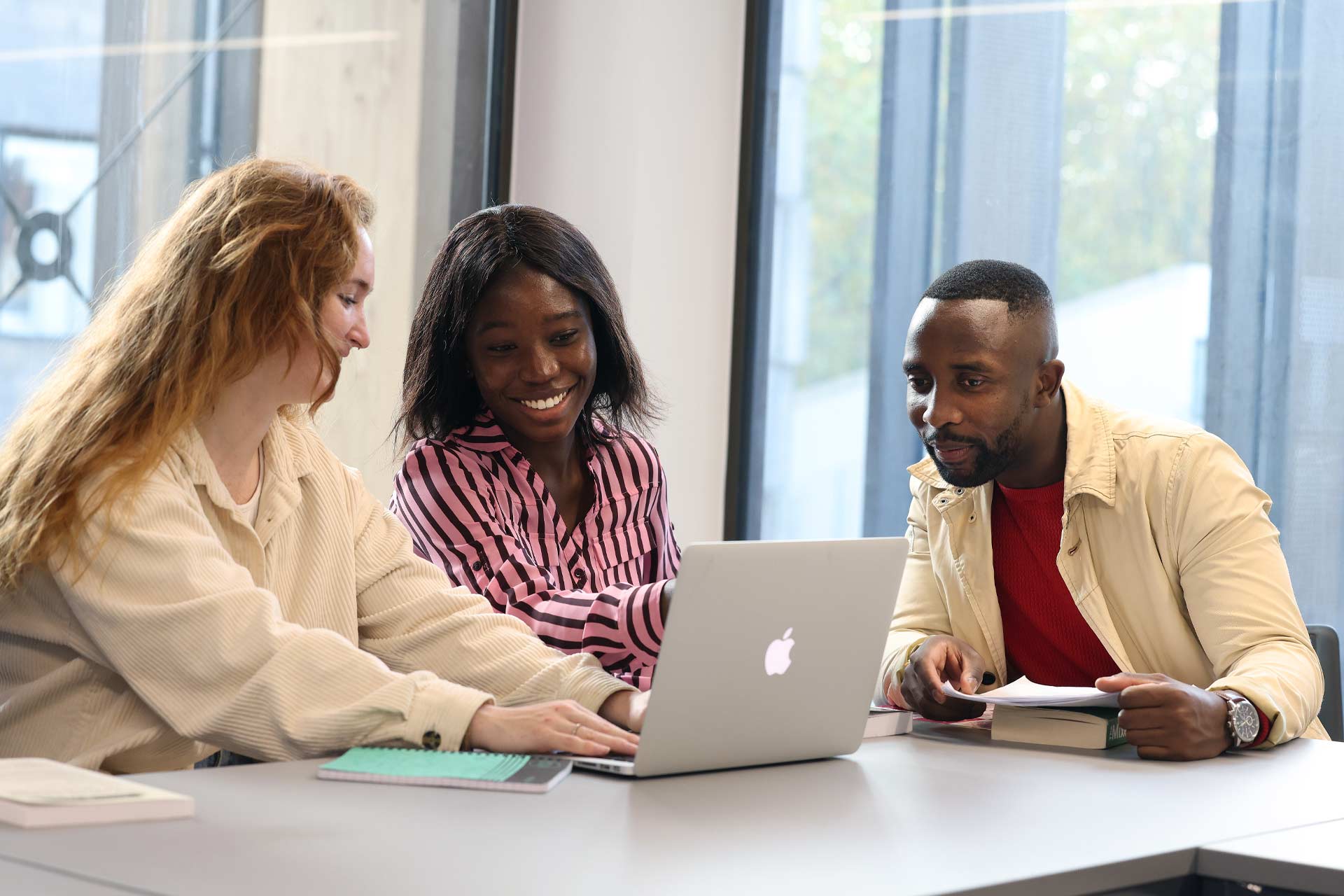 three students sat around a table studying with a laptop