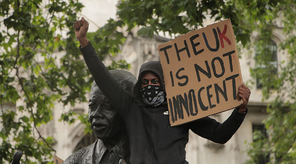 Man holding sign saying 'The UK is not innocent' during Black Lives Matter protest