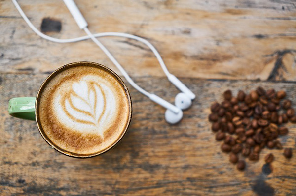 Mug of coffee and headphones on wooden table.