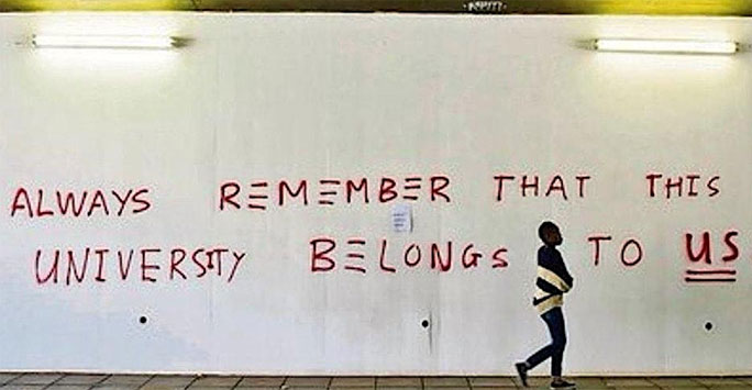 A woman walking past a wall with 'Always remember that this university belongs to us' written on it.