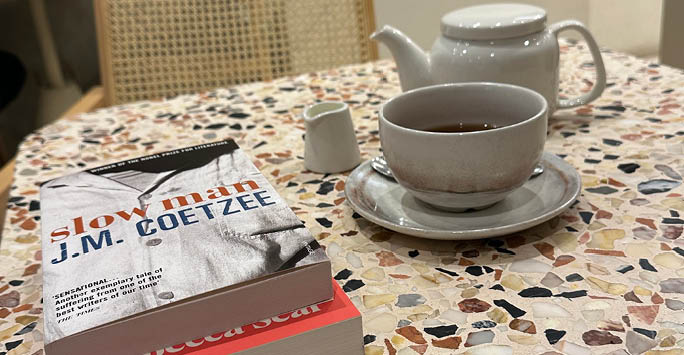 A cup of tea and tea pot next to books.