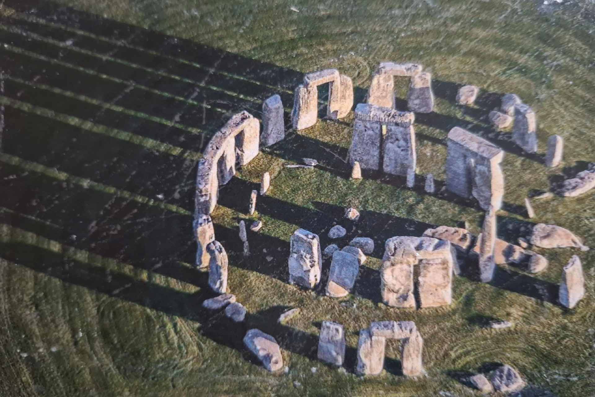 A stone circle on grass with shadows being cast from the sun