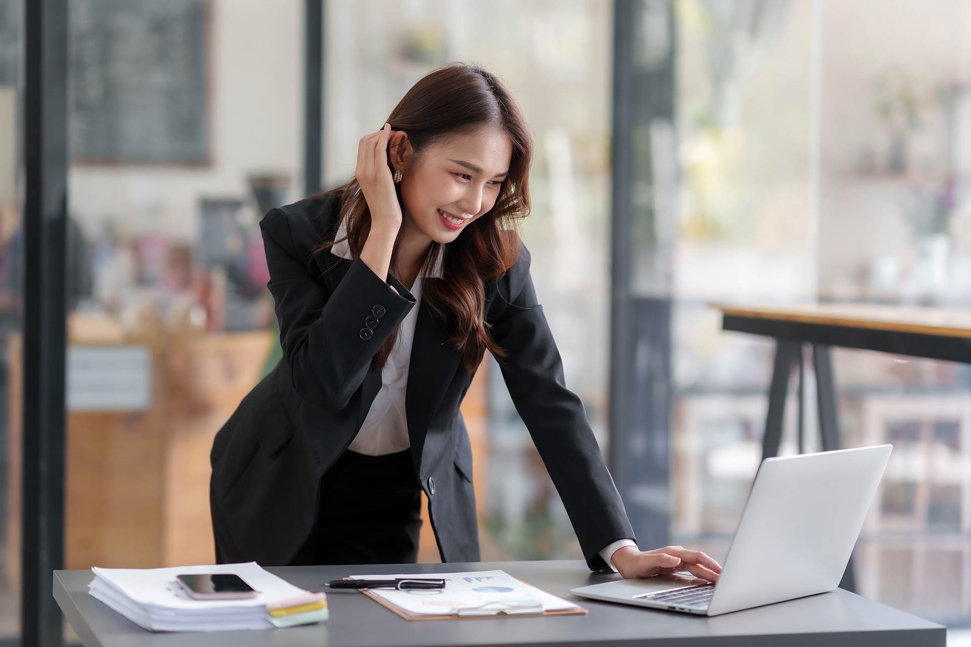 A business professional stands by a desk while working on a laptop.