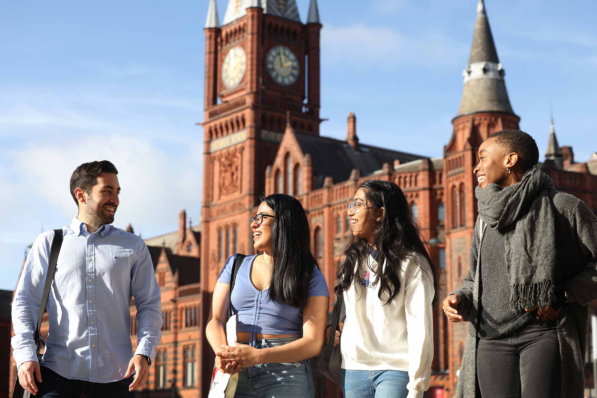 Four students standing talking in University Square, with the Victoria Gallery & Museum behind them.