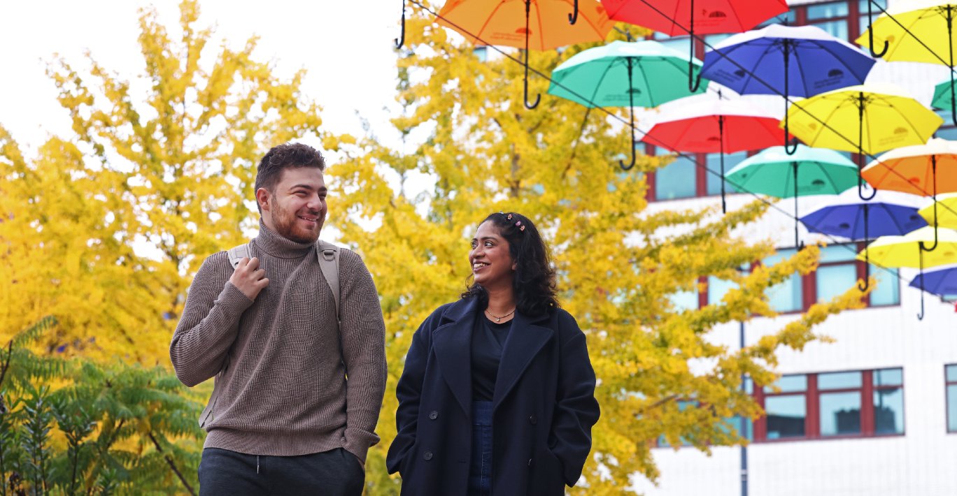 Two students are walking across University Square with the umbrella display in the background.