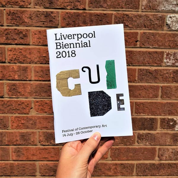 Someone holding the Biennial Guide with an exposed brick background