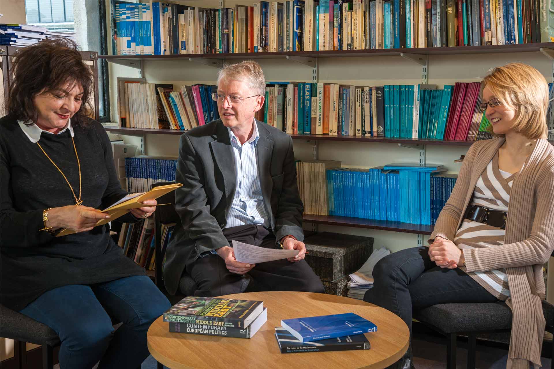 Three academics sit in the library with Politics literature