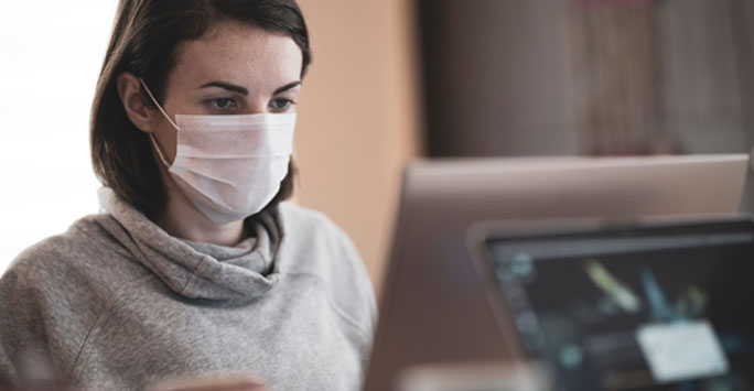 Woman wearing a medical mask writing on a laptop