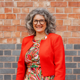 A woman with curly hair and a bright jacket smiling