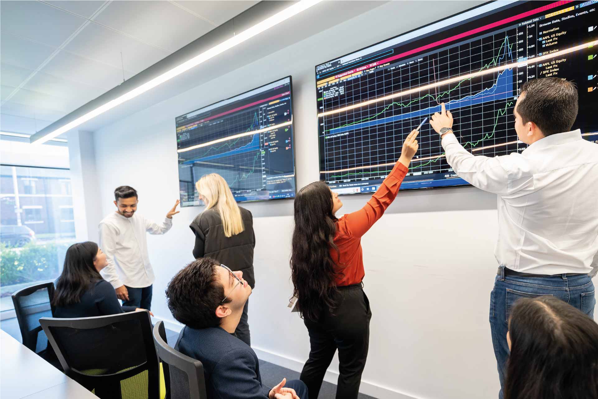 MSc students in McKenzie Trading suite looking at screens and talking to each other