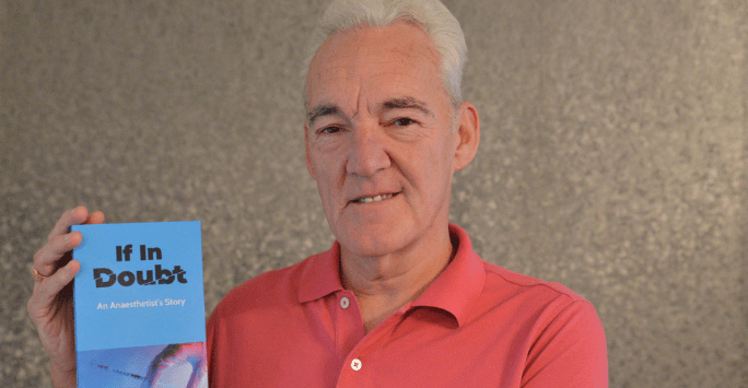 man in polo shirt holds up a copy of his book