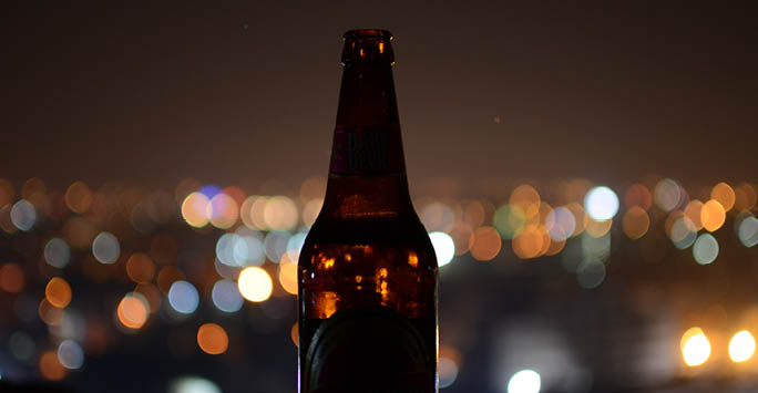 Beer bottle sat on a table with lights in the background.