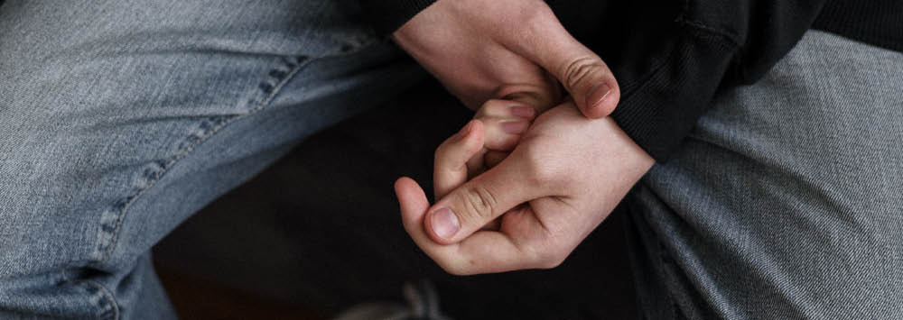 A close up of hands held, rested on dark blue jeans.