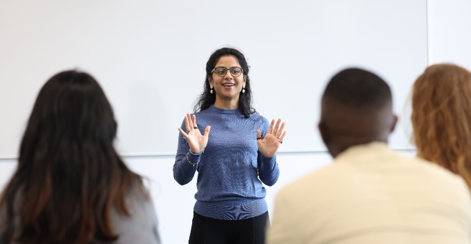 A postgraduate student teaching at the front of a class of students