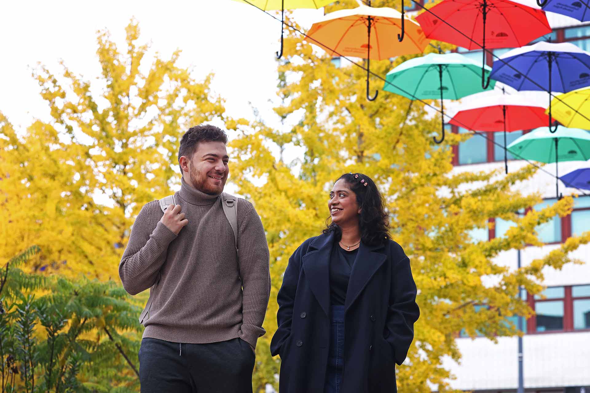 Two students walking in University Square, under a colourful display of umbrellas.