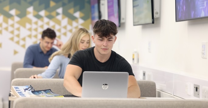 A student is sitting in a lecture theatre, using a laptop.